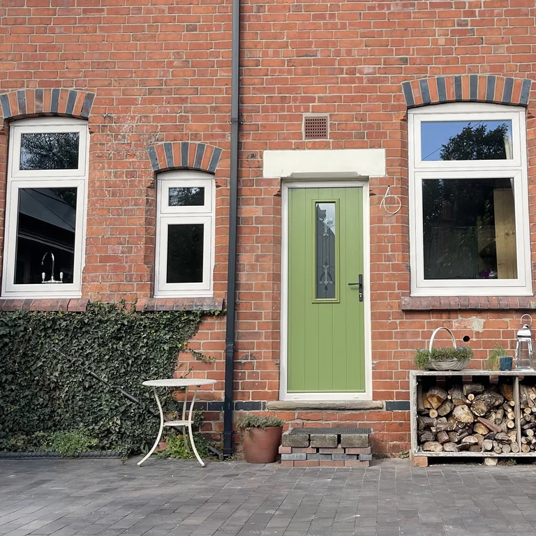 White-framed windows and green door on a red-brick house — Double Glazing Plus installation
